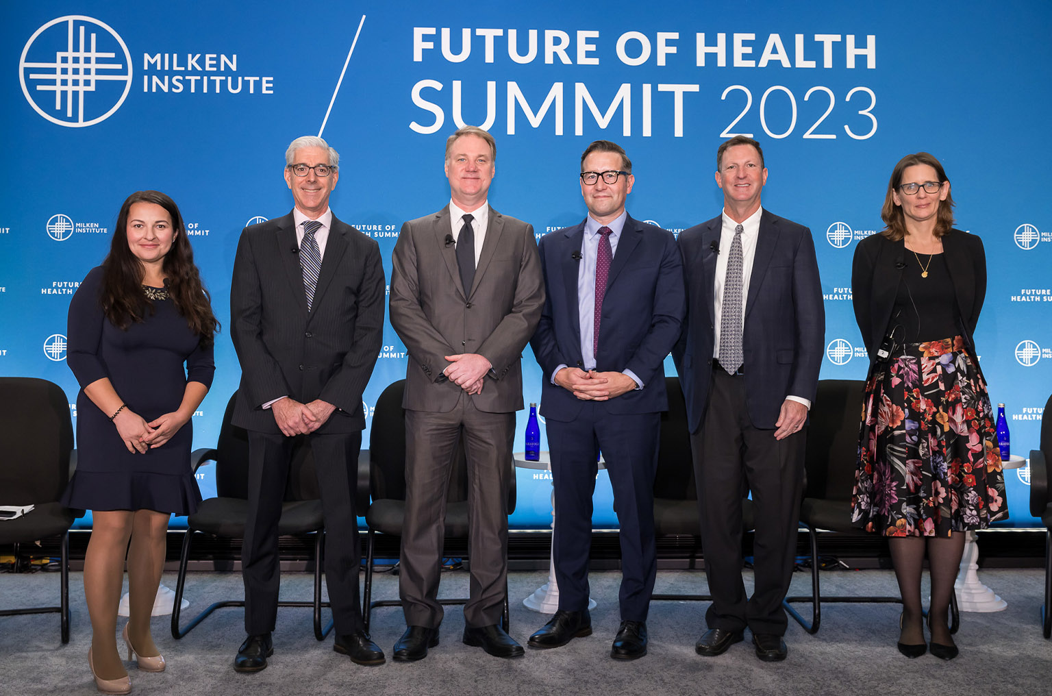 Six people posing for a portrait in front of screen reading "Milken Institute Future of Health Summit 2023"